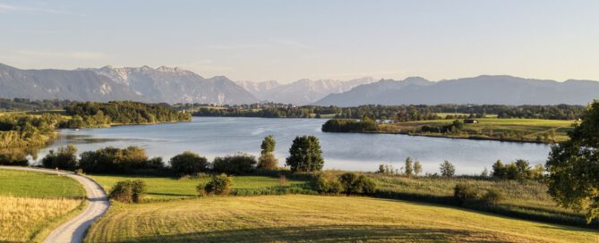 Feldweg, der durch Wiesen zum Riegsee führt, im Hintergrund die Alpen