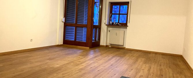 Leerer Wohnraum mit neu verlegtem Parkett und großen Fenstern