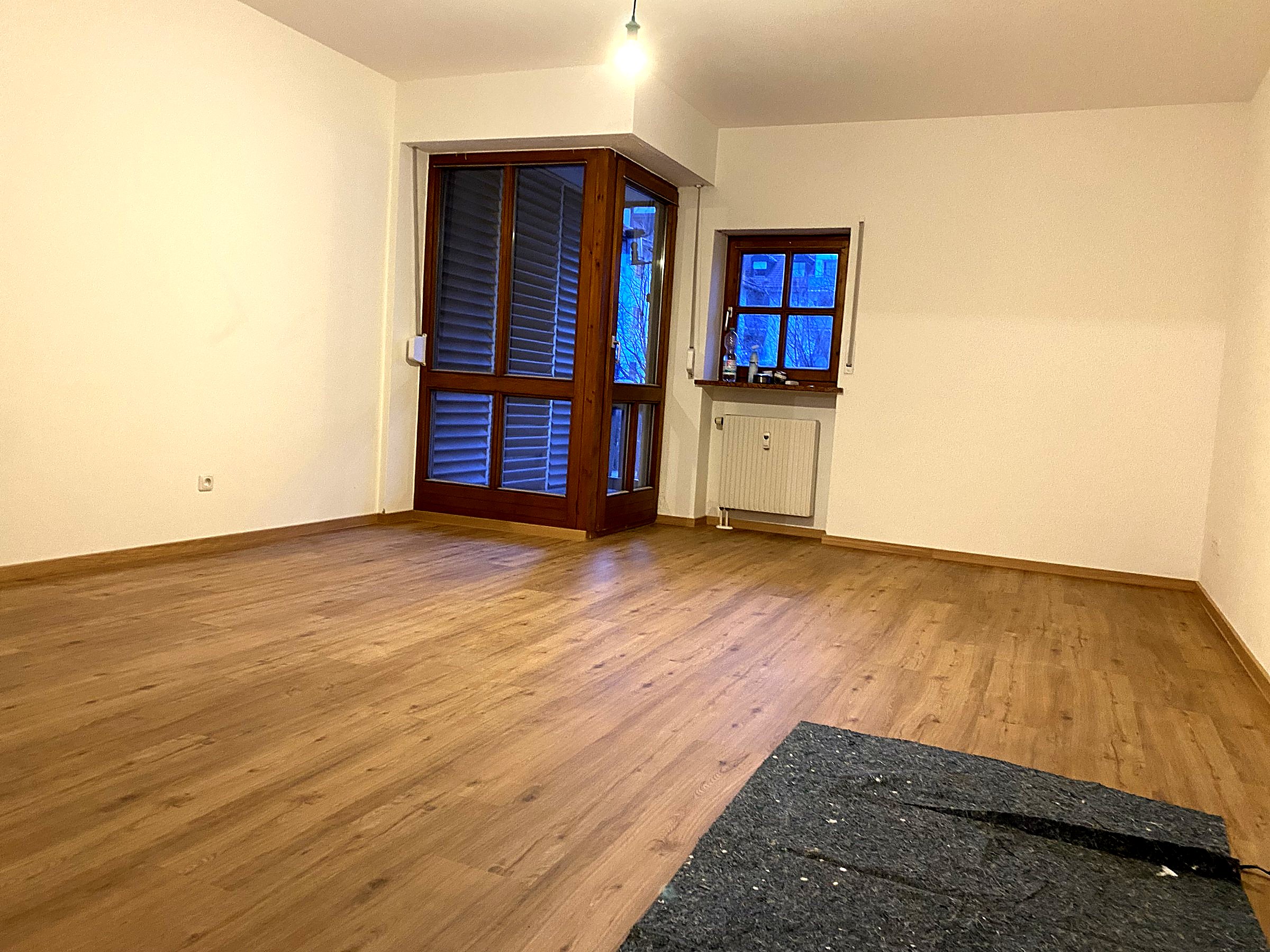 Leerer Wohnraum mit neu verlegtem Parkett und großen Fenstern