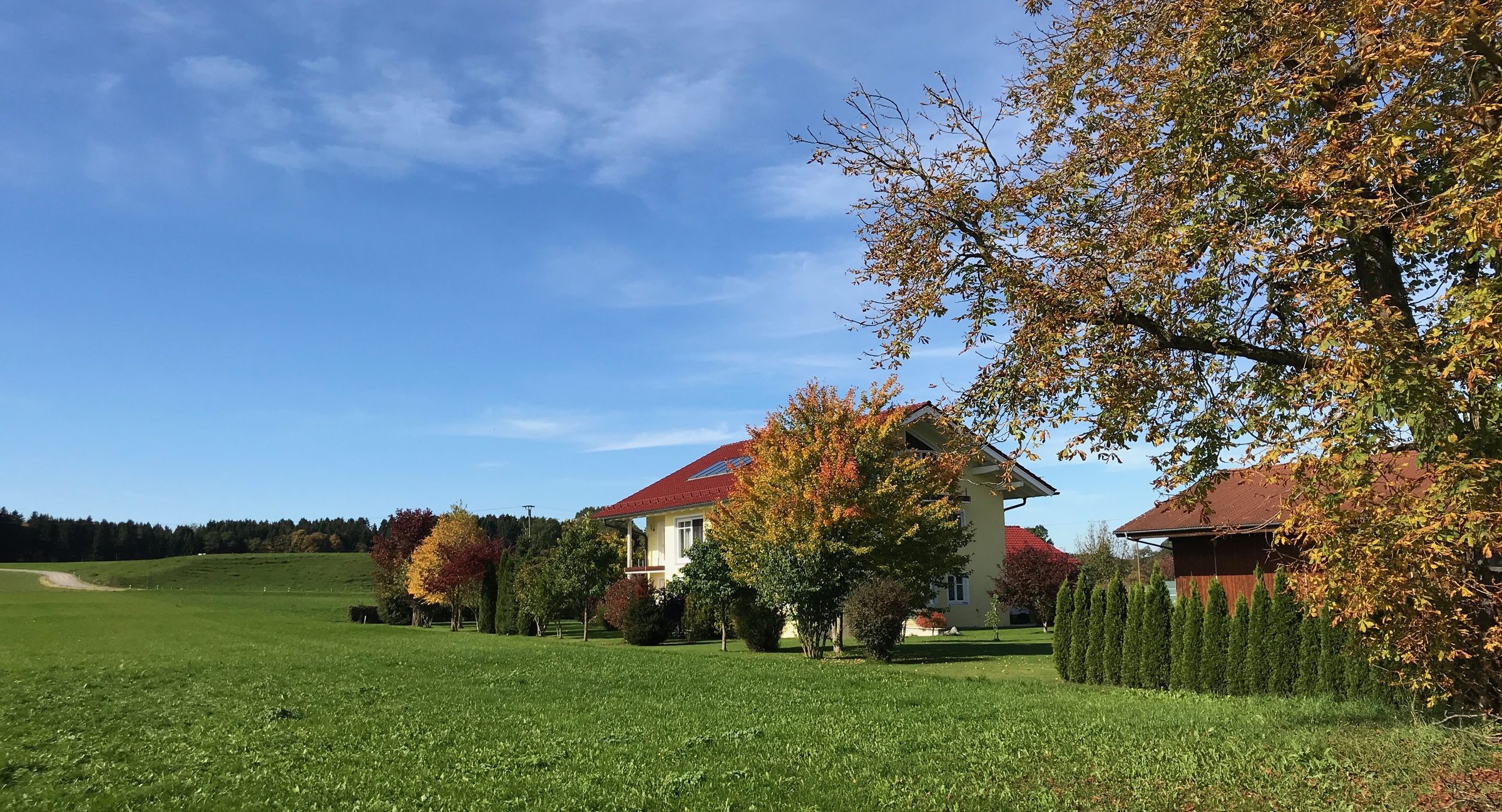 Wohnhaus im oberbayerischen Voralpenland an einem Herbsttag, Wiese und Bäume im Vordergrund